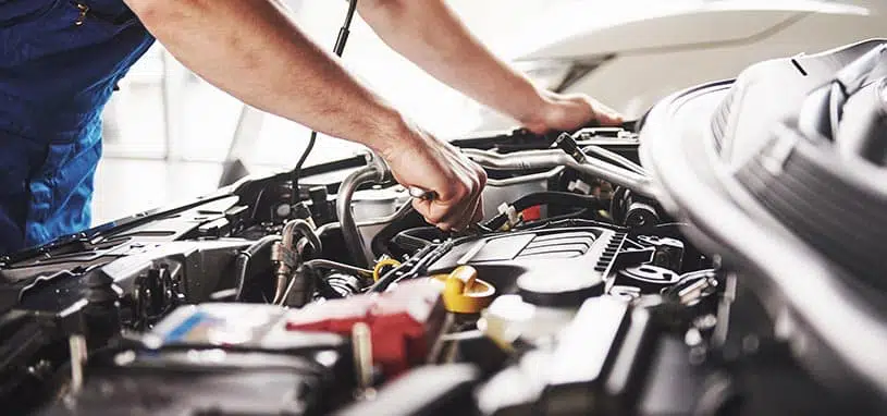 Mechanic carrying out air conditioning repairs in a vehicle engine bay.