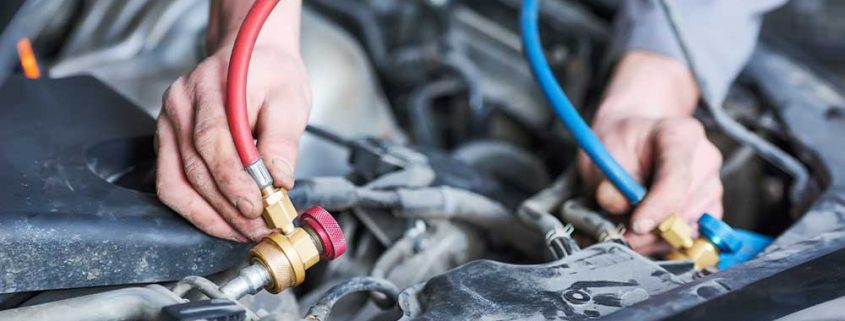 A closeup picture of a mechanic’s hands as they regas a vehicle’s air conditioning system.