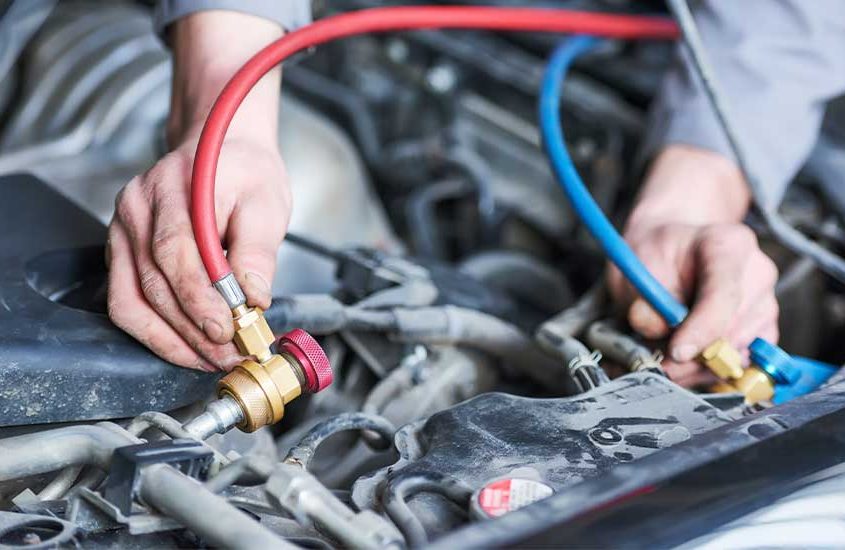 A closeup picture of a mechanic’s hands as they regas a vehicle’s air conditioning system.