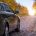 Car driving along a leaf-covered road in autumn.