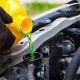 A Mechanic wearing red gloves is pouring bright green engine coolant into a car radiator under the bonnet to keep the cooling system at a safe operating temperature.