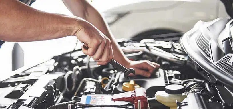 Mechanic carrying out air conditioning repairs in a vehicle engine bay.
