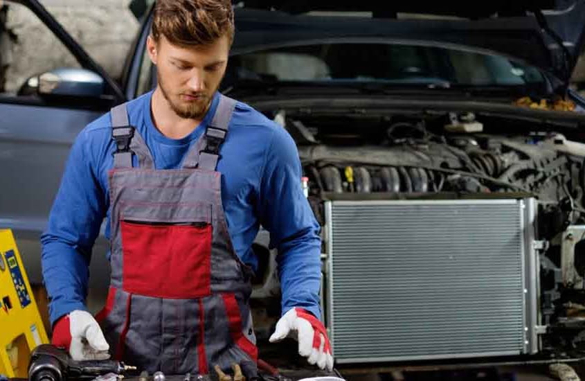 Mechanic inspecting car radiator for EV battery thermal management and cooling system service.