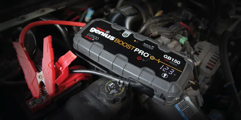 Portable jump starter connected to a car battery in an engine bay.