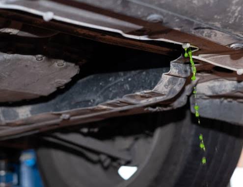 Close-up of green coolant leaking from under a car radiator, showing signs of a leaking radiator and cooling system damage.