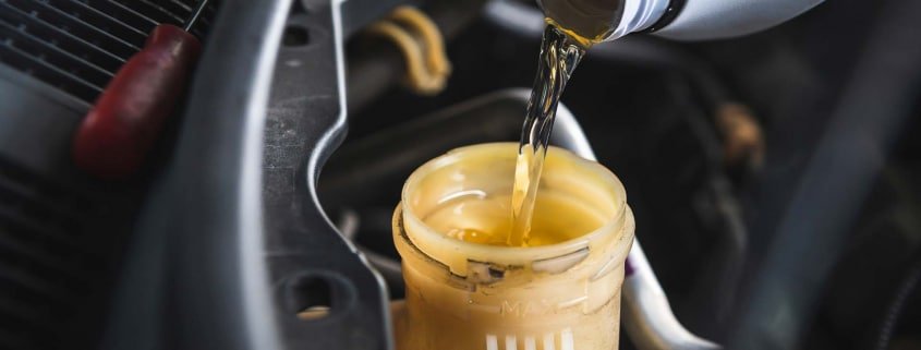 Closeup of a mechanic pouring fresh, clear brake fluid into the master cylinder of a vehicle.