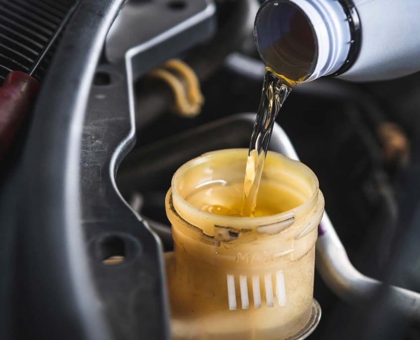 Closeup of a mechanic pouring fresh, clear brake fluid into the master cylinder of a vehicle.