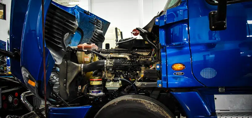 Blue semi-truck undergoing engine and radiator inspection in a workshop.