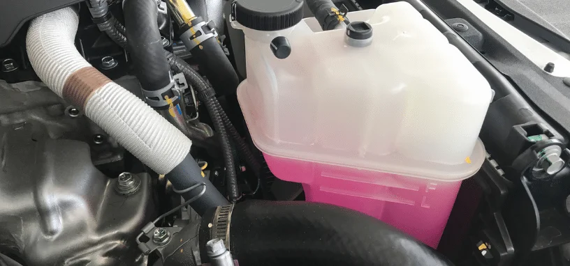Coolant reservoir filled with pink coolant in a modern vehicle engine bay.