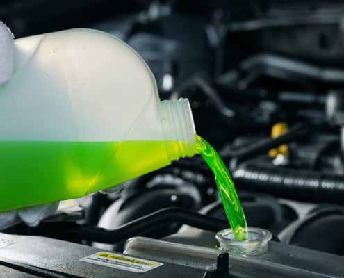 A mechanic pouring coolant directly into a car’s radiator