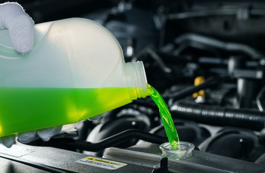 A mechanic pouring coolant directly into a car’s radiator
