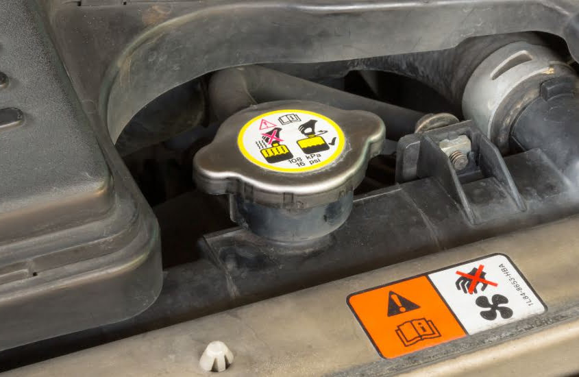 A closeup of a clearly marked radiator cap within a car.