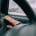 A hand hovers over a car dashboard vent to check the heater airflow, seen through a steering wheel on a snowy day.