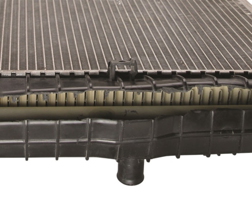 A car radiator with a badly cracked and broken black plastic tank on the bottom edge, isolated against a white background.