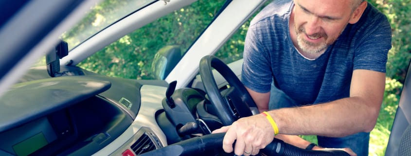 Man hoovering air vent in car