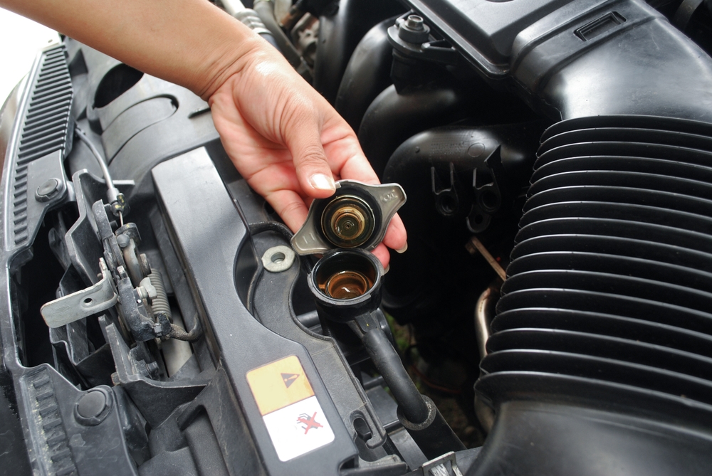 Hand opening a car radiator cap to check coolant levels under the hood.