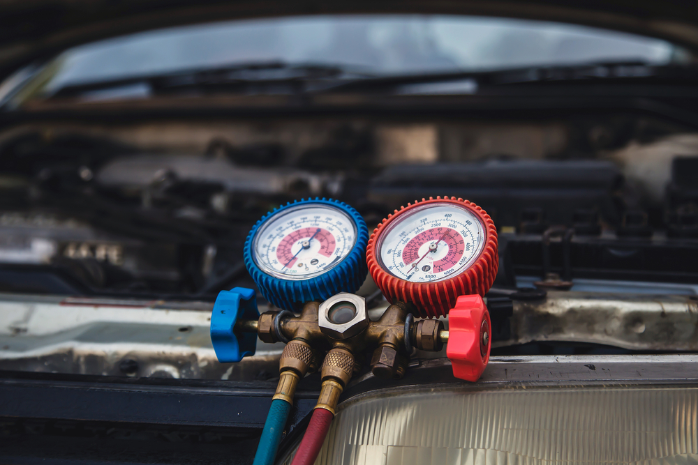 Mechanic using a manifold gauge set to check and service a car’s air conditioning system.