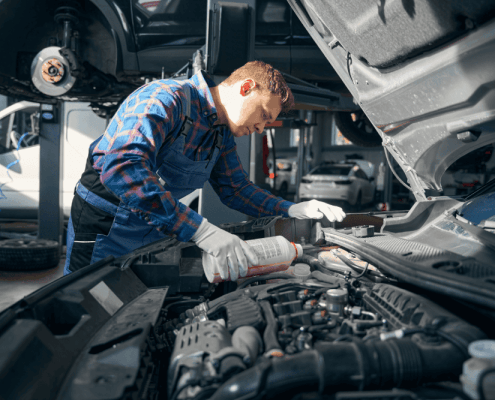 Mechanic pouring coolant into a car’s cooling system while performing maintenance under the bonnet in a professional auto repair workshop.
