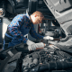 Mechanic pouring coolant into a car’s cooling system while performing maintenance under the bonnet in a professional auto repair workshop.