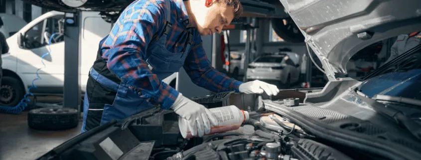Mechanic pouring coolant into a car’s cooling system while performing maintenance under the bonnet in a professional auto repair workshop.