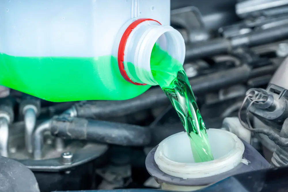 A stream of green coolant is poured from a plastic container into a car's radiator reservoir.