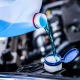 Green engine coolant being poured from a white container into a car’s coolant reservoir under the hood.