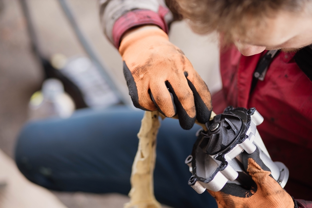 Mechanic wearing protective gloves inspecting and cleaning a car water pump, focusing on the impeller and housing components.