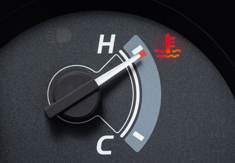 Close-up of a car temperature gauge with the needle in the red zone, indicating engine overheating, accompanied by an illuminated high-temperature warning light.