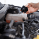 Close-up of a car engine with a hand opening the coolant reservoir cap, showing the cooling system components under the bonnet.