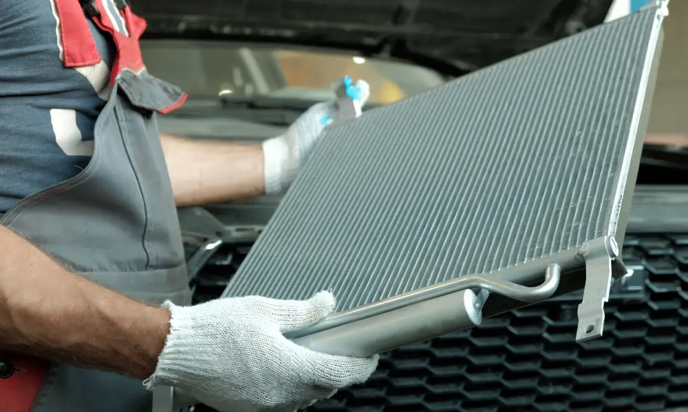 Mechanic holding a car radiator in front of a vehicle during replacement or repair process.