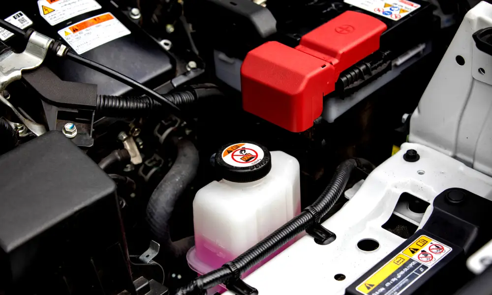 Close-up of a car engine showing the coolant reservoir and battery components under the hood.