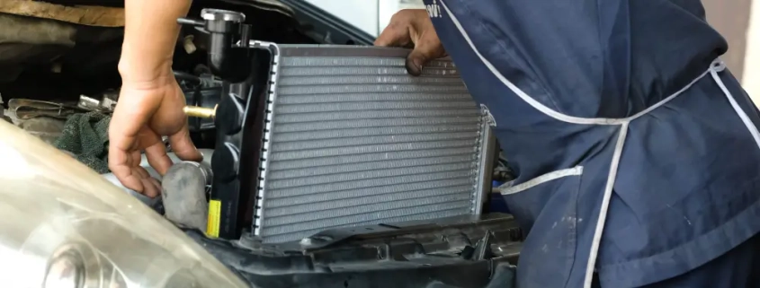 Mechanic installing a car radiator in the engine bay during vehicle maintenance.