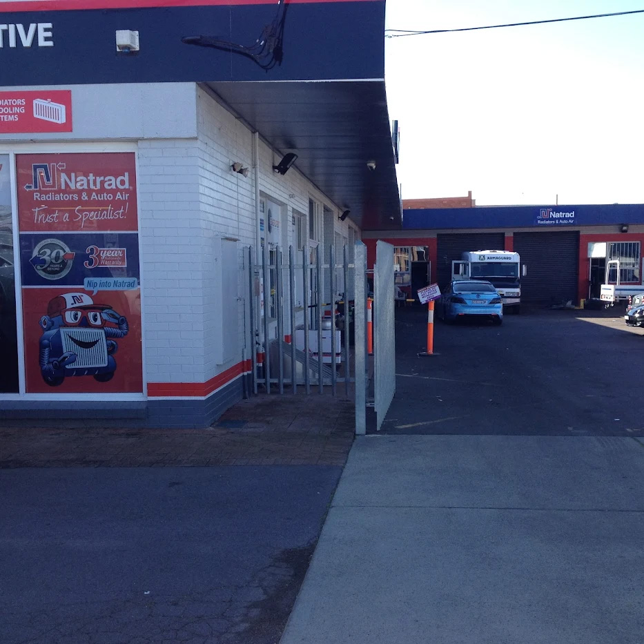 Exterior view of a Natrad service centre with red and blue branding, a gated side entrance, and cars parked in the driveway.